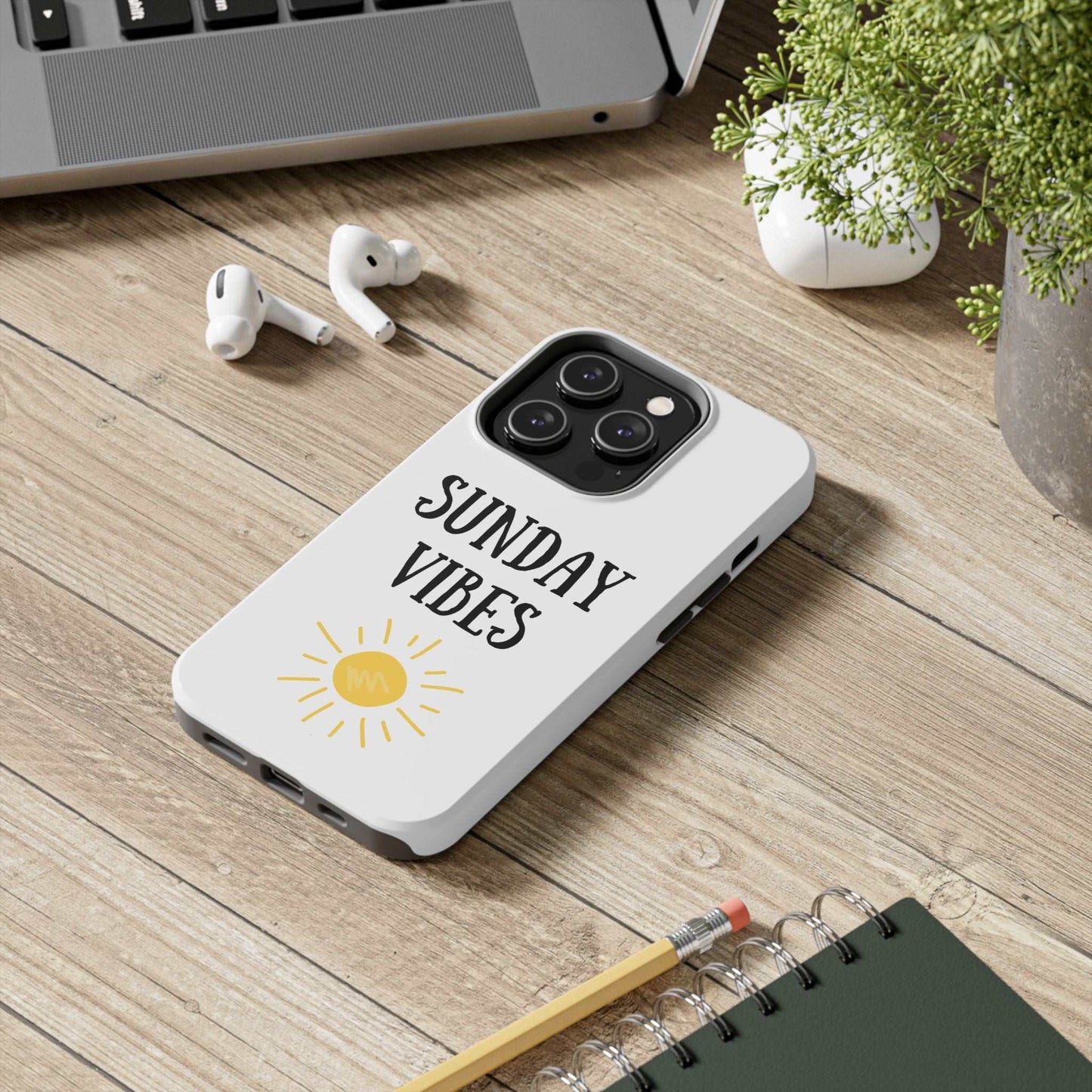 'Sunday Vibes' sun graphic phone case on a wooden desk with accessories, featuring durable Lexan plastic and glossy finish.