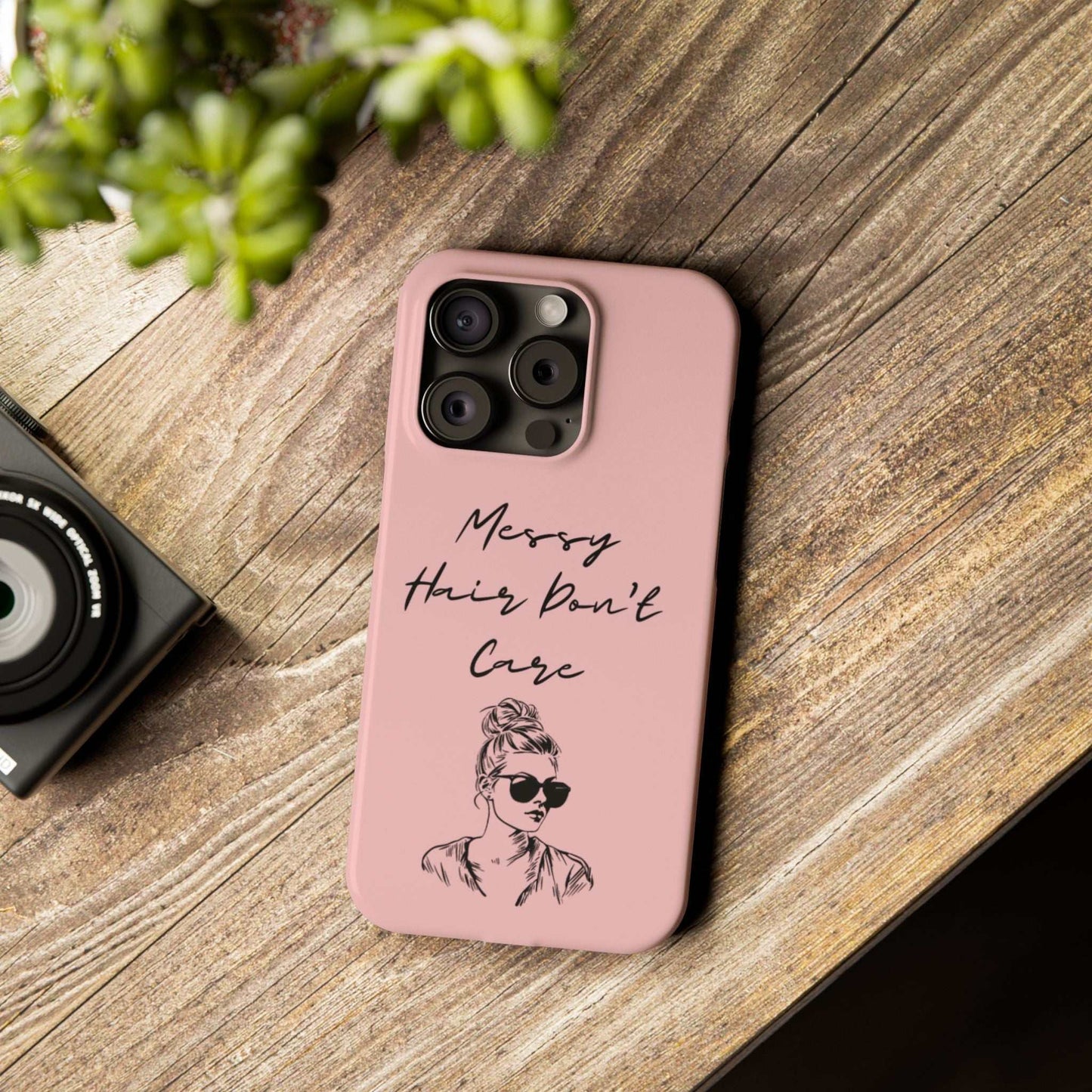 Baby pink phone case with "Messy Hair, Don't Care" quote, featuring a trendy girl in sunglasses and a messy bun, on a wooden surface.