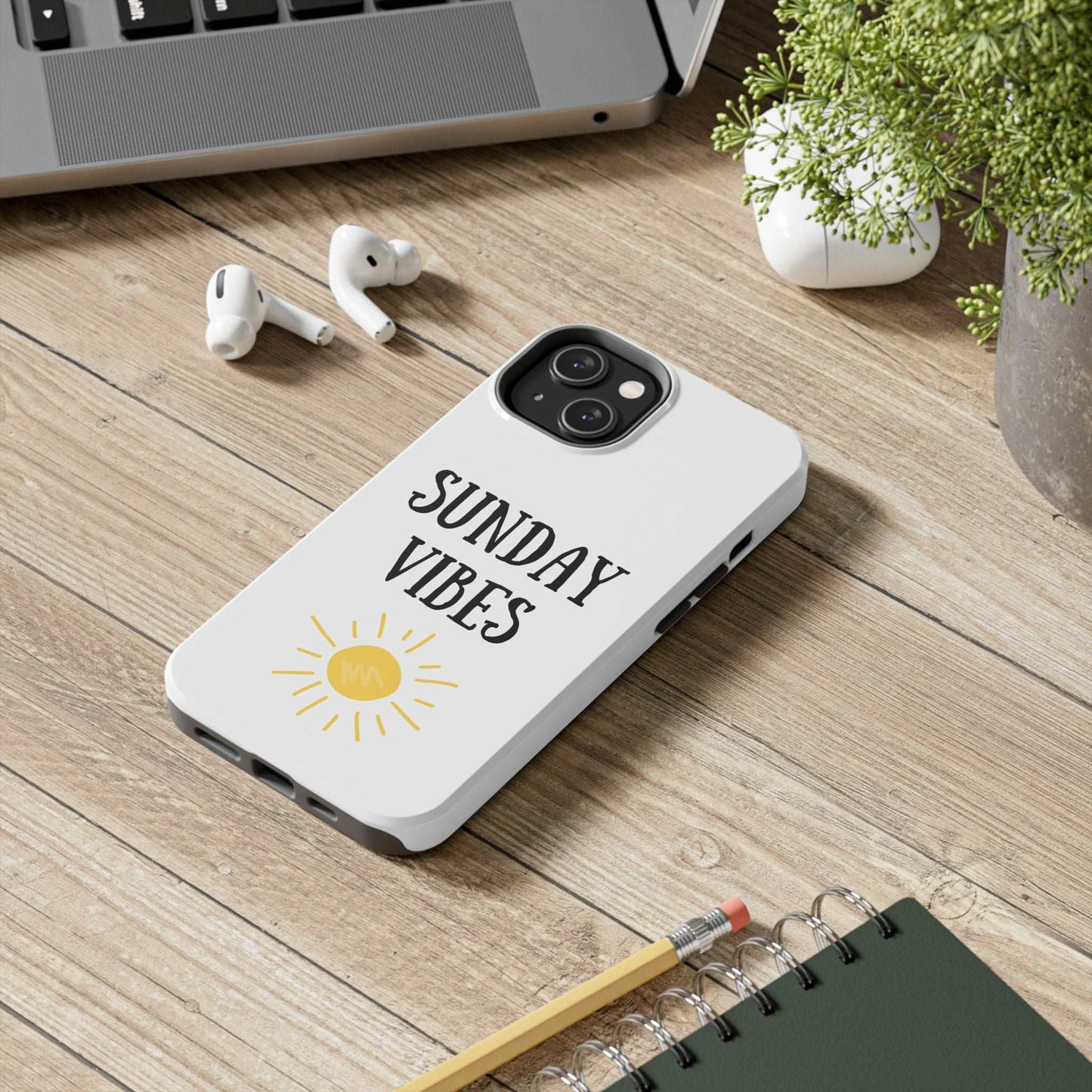 'Sunday Vibes' sun graphic design phone case on wooden desk with accessories.