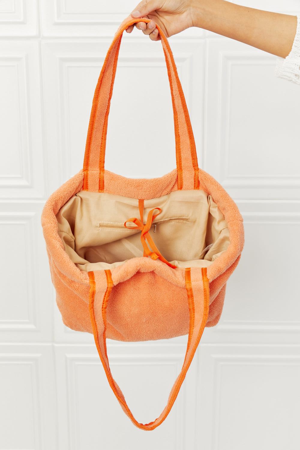 Orange plush 'Paradise Tote Bag' with long straps and interior pockets.