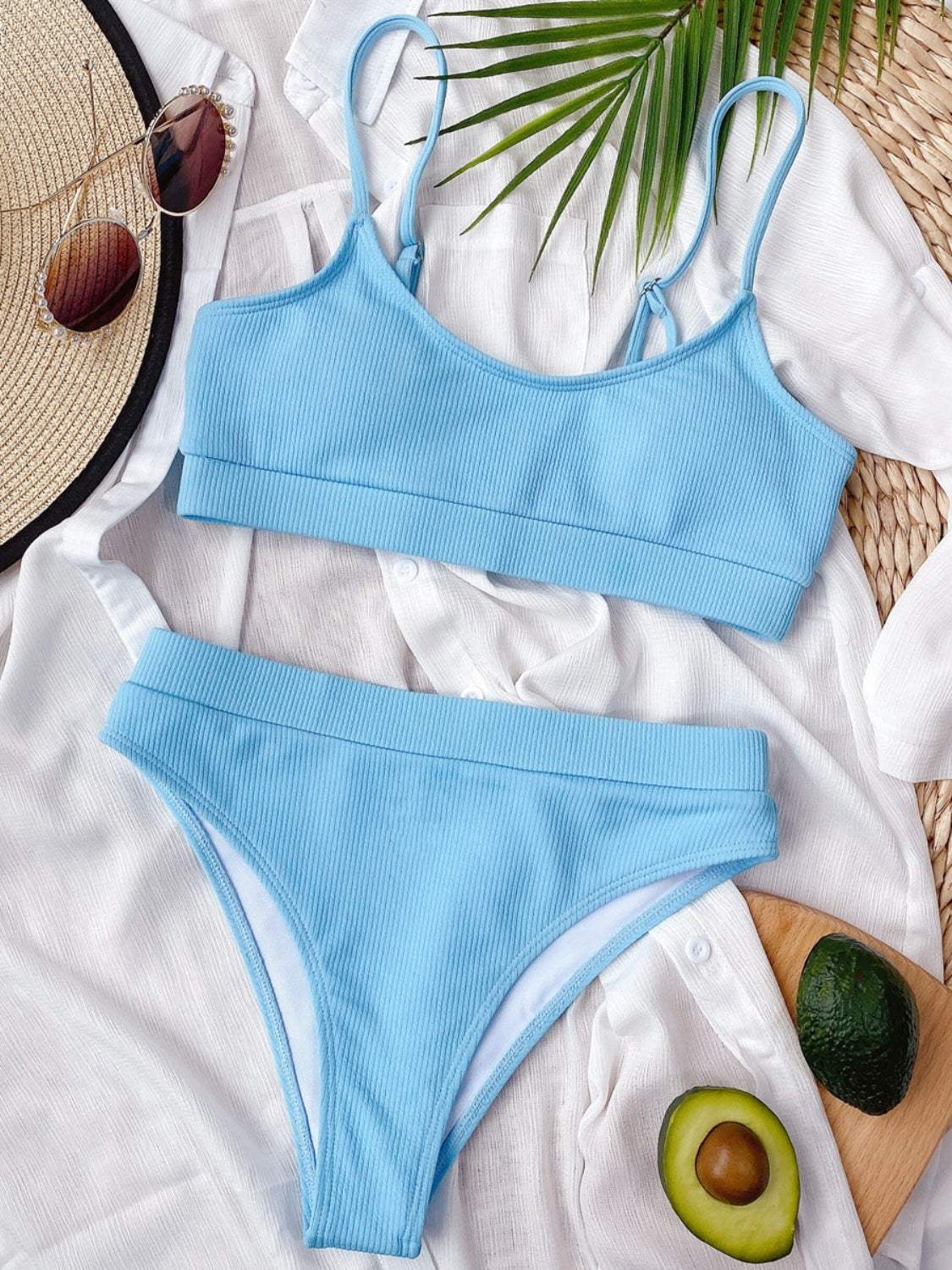 Scoop neck spaghetti strap two-piece swim set with removable padding, blue color, laid on white fabric.