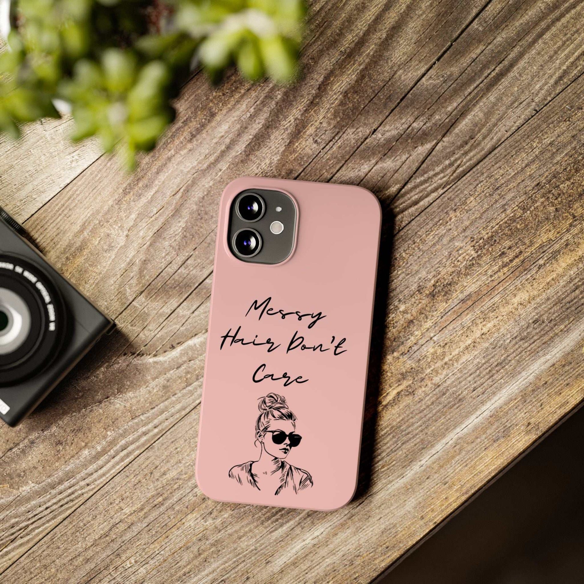 Baby pink phone case with "Messy Hair, Don't Care" text and girl graphic, on a wooden surface.