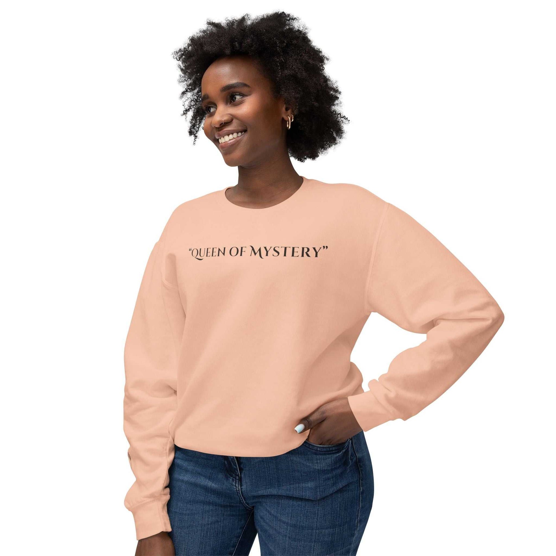 Queens Mystery Sweatshirt featuring "Queen of Mystery" text in peach color worn by a smiling person.