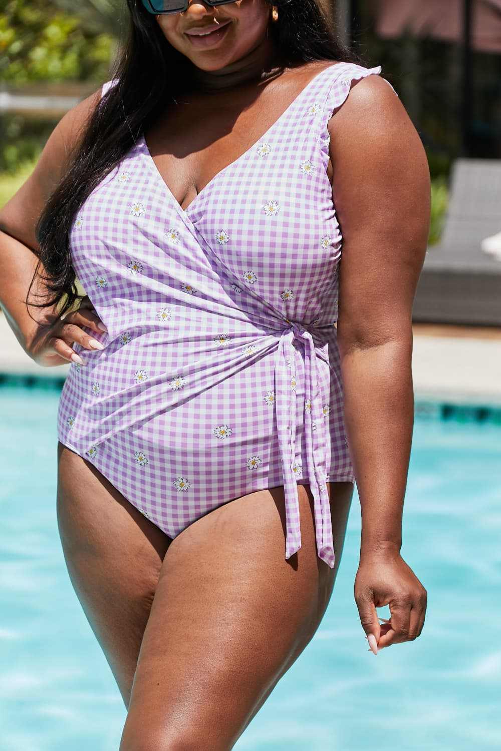 Plus size woman wearing Marina West Swim Full Size Float On Ruffle Faux Wrap One-Piece swimsuit in purple plaid design by a pool.