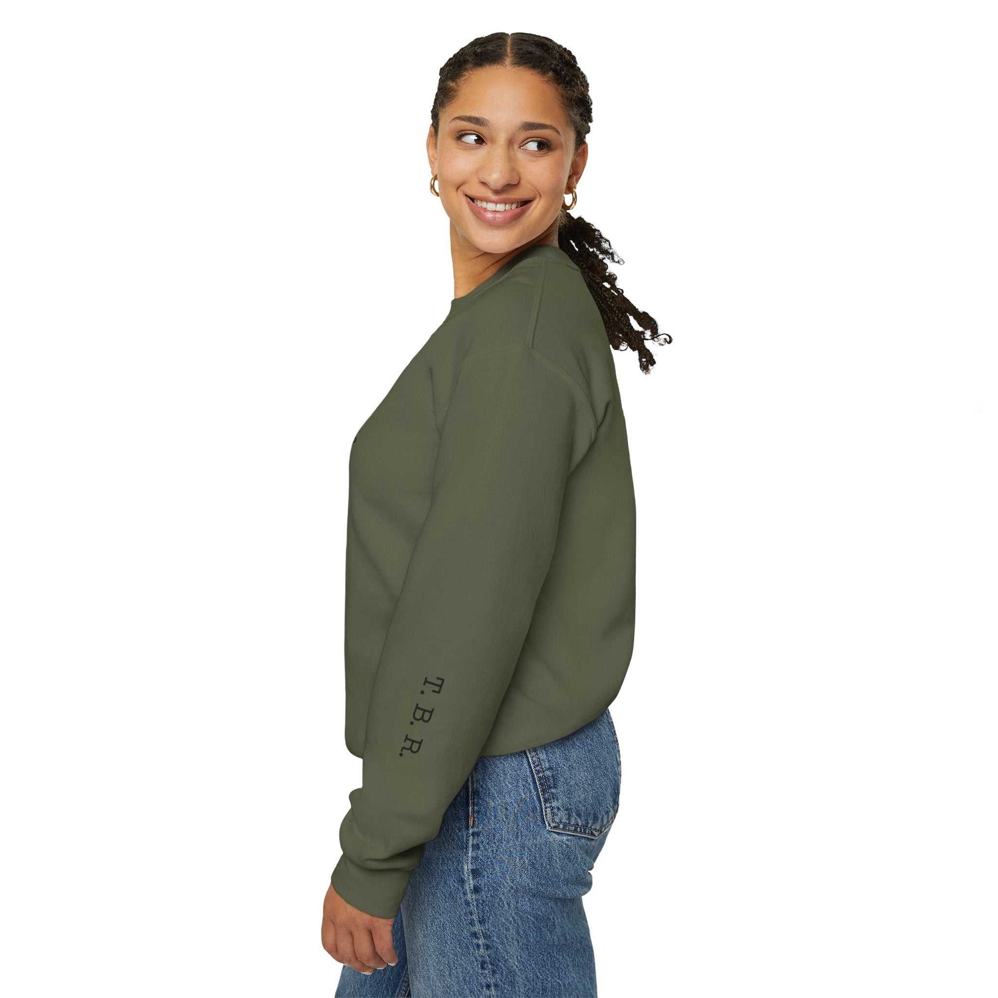 Tsundoku crewneck sweatshirt with "T.B.R." on the sleeve, worn by person smiling.