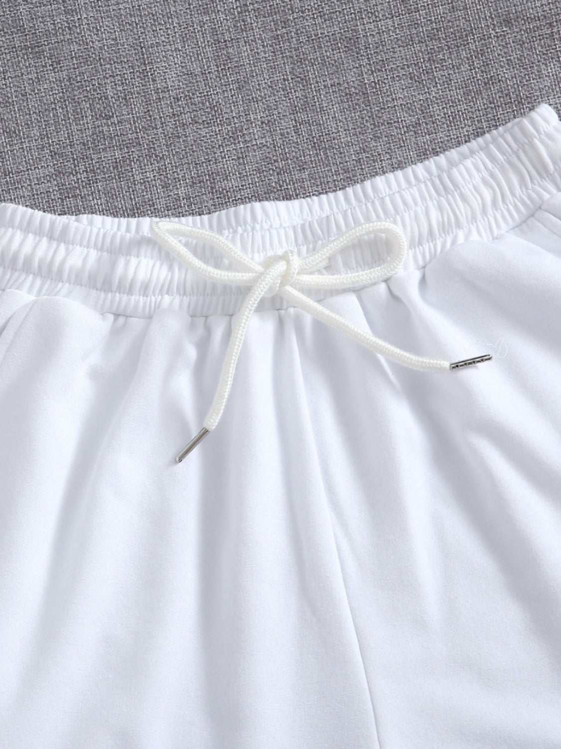 White drawstring pocketed elastic waist shorts on gray background.