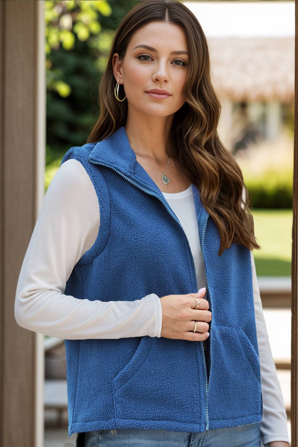 Blue zip up vest coat with pockets, worn over a long-sleeve white top.