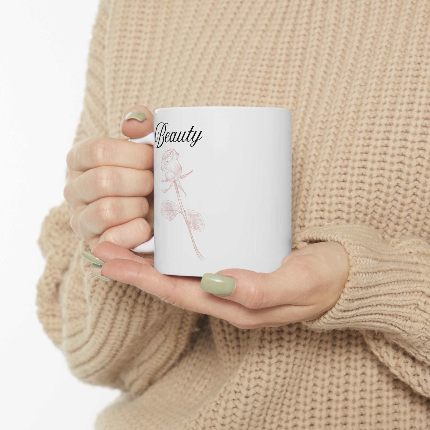 Ceramic mug with "Beauty" text and dusty rose design, held by person in beige sweater.