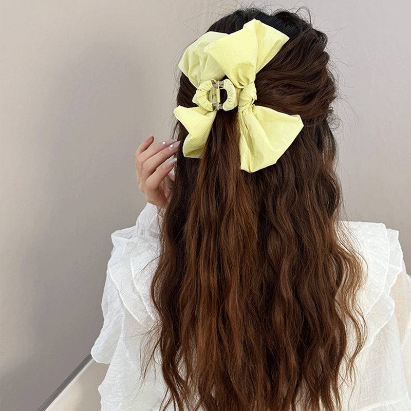 Bow Hair Claw Clip in yellow polyester, 5.1 inches long, worn in wavy brown hair.