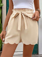 Perfee Frill Tied Shorts with Pockets in beige, featuring a tied waistband and scalloped hem.