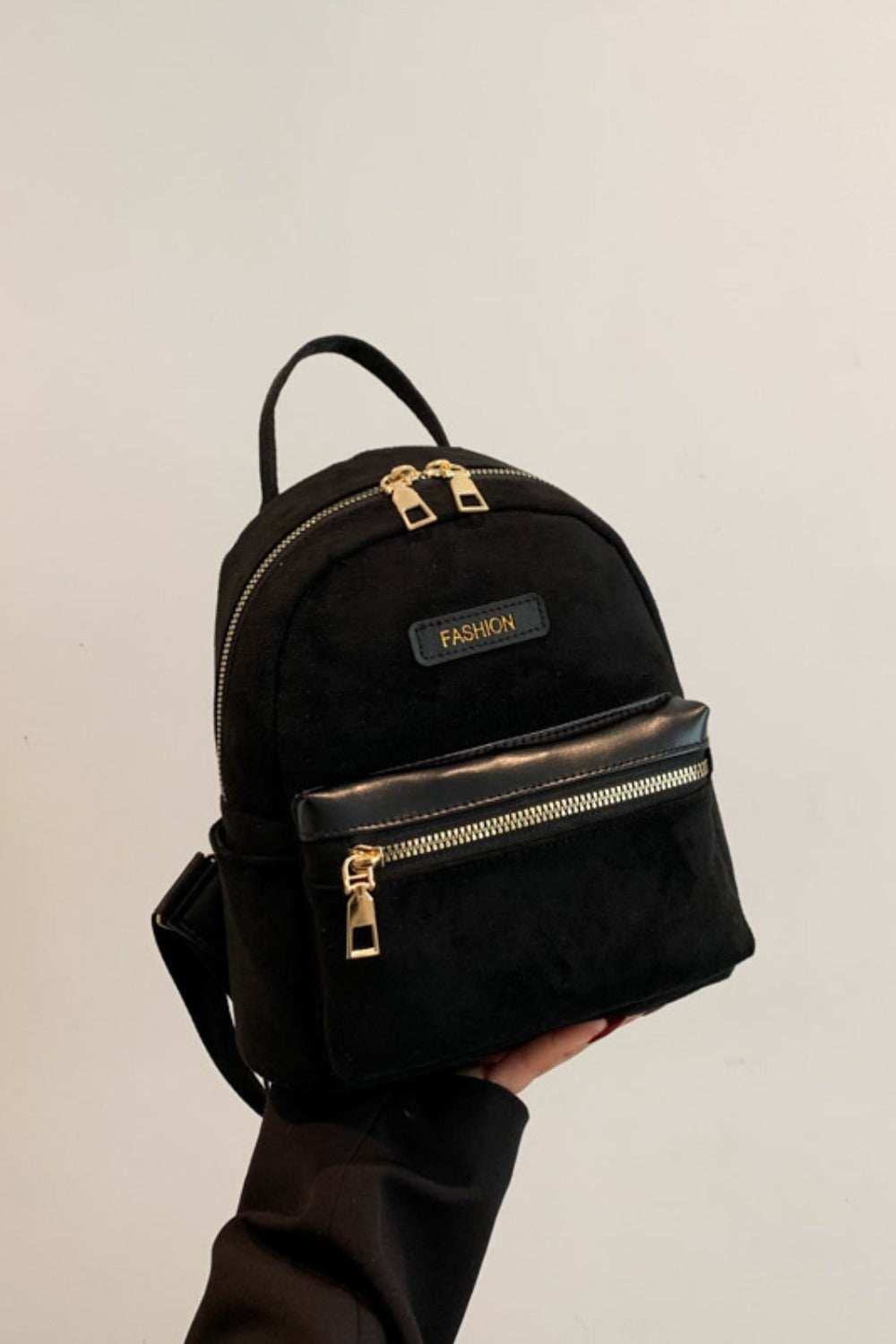 Small black suede backpack with adjustable straps and gold zippers.