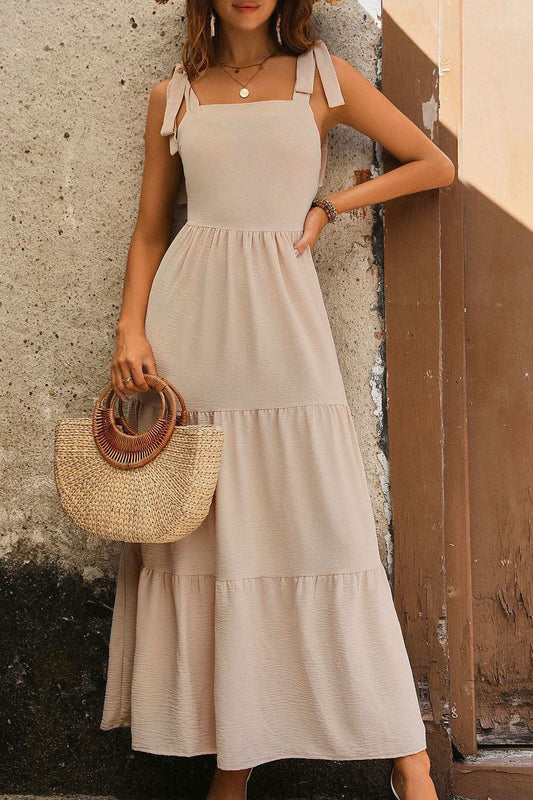 Perfee Tie Shoulder Smocked Tiered Dress in beige, sleeveless with bow tie straps, and a flowy tiered design.