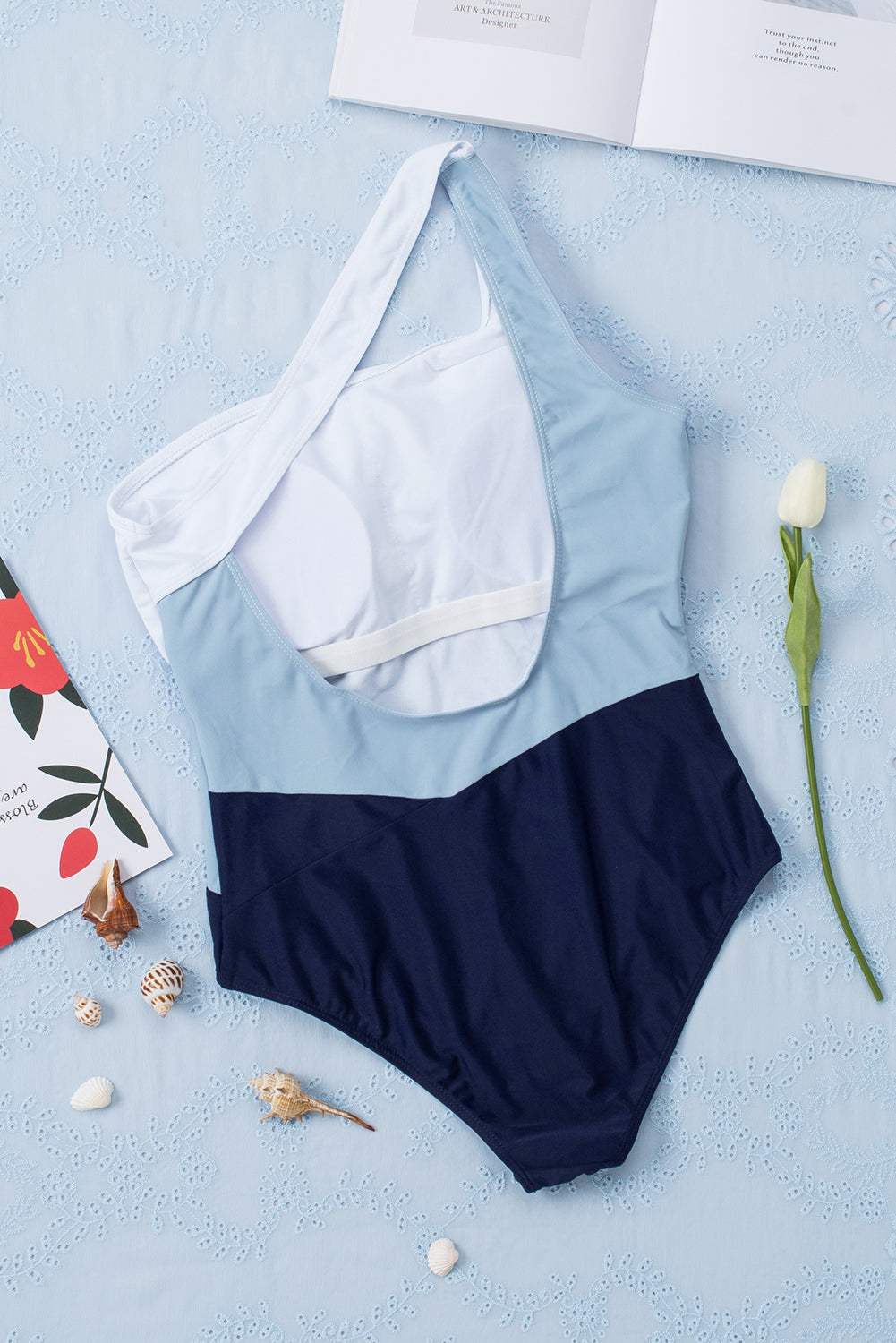 Full size cutout color block sleeveless one-piece swimwear on display with seashells and flower accents.