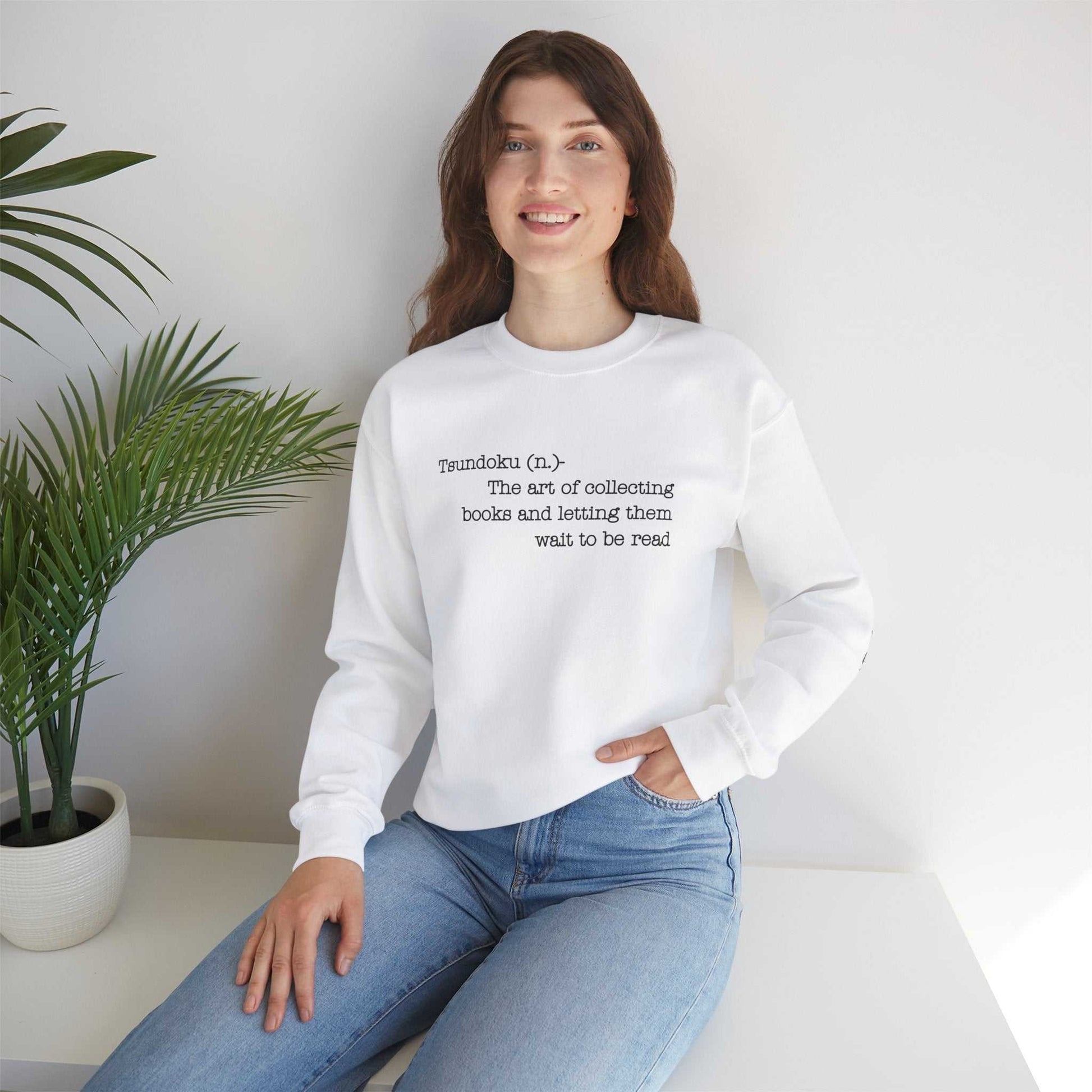 Tsundoku crewneck sweatshirt with book collecting definition, worn by woman indoors.