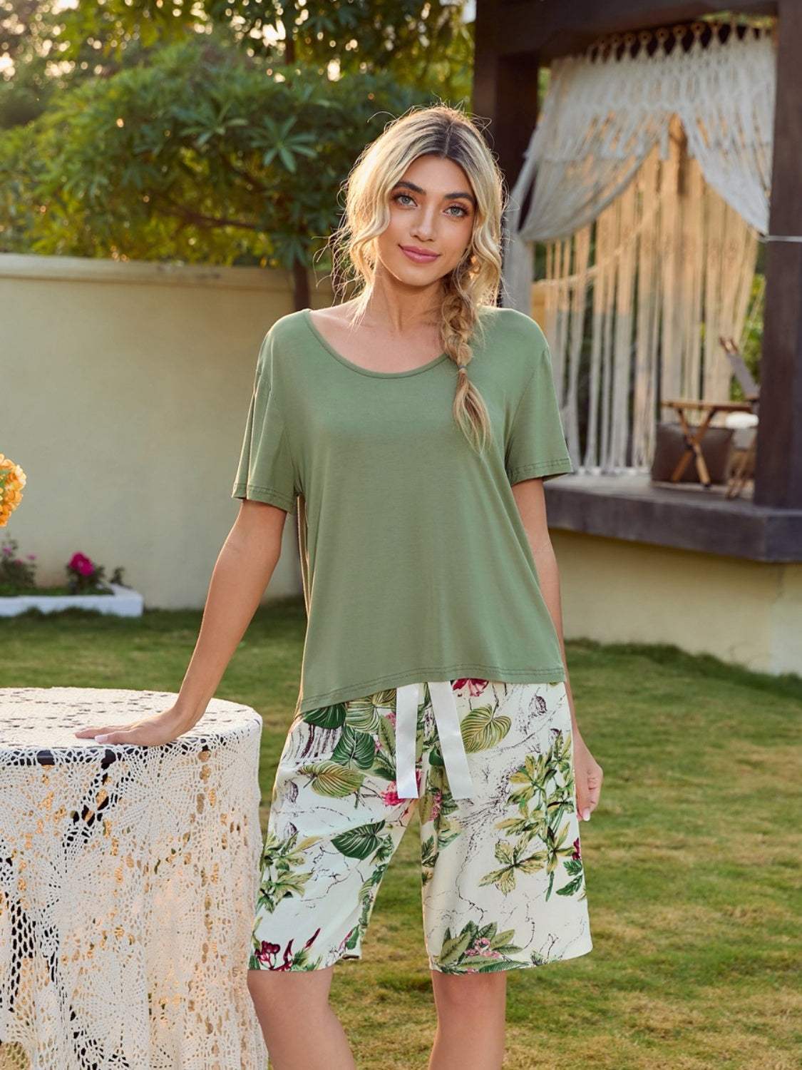 Woman wearing a short sleeve top with printed shorts lounge set in a garden setting.