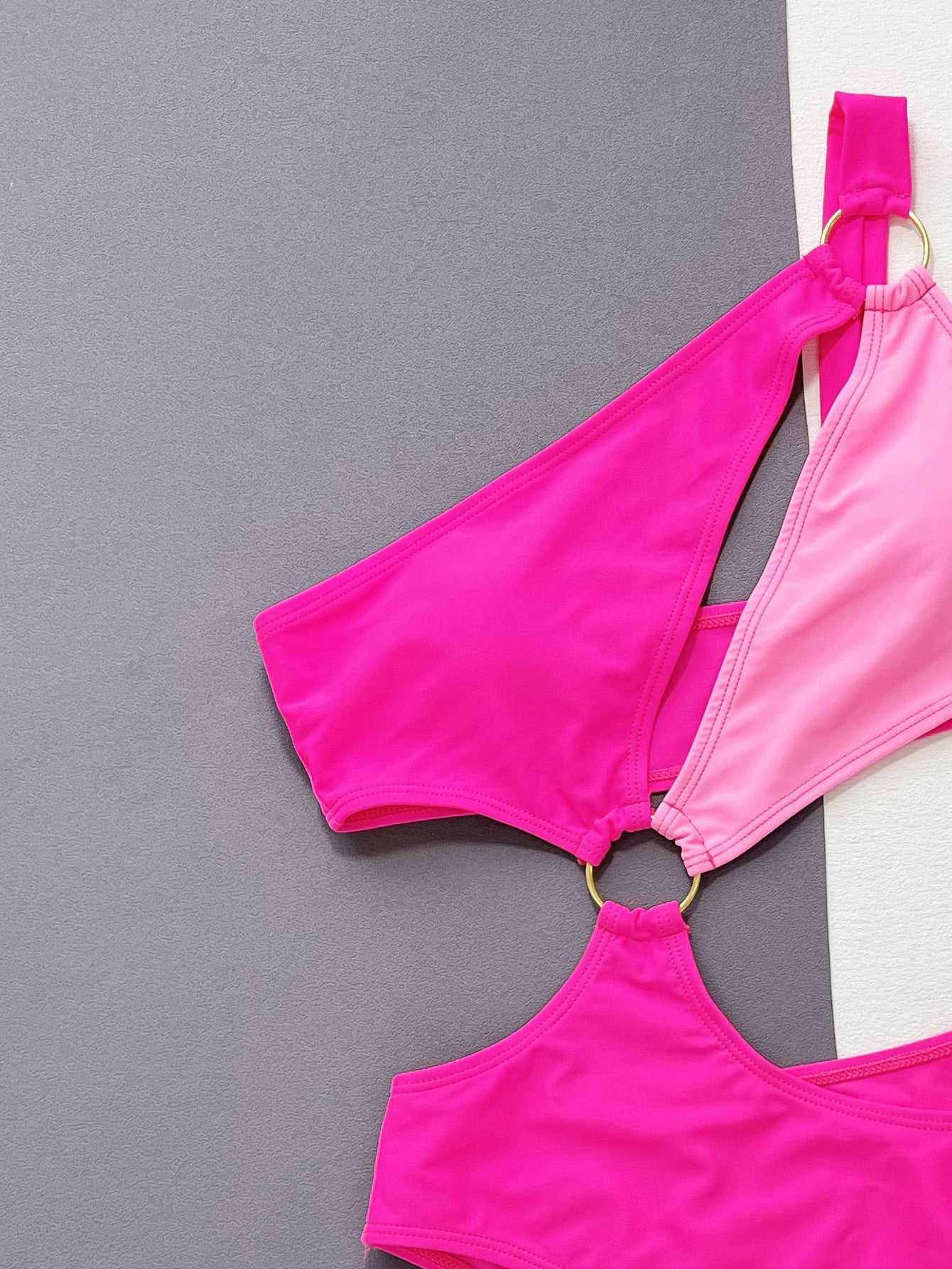 One-shoulder cutout ring detail one-piece swimsuit in pink with contrast pattern and grommet features.