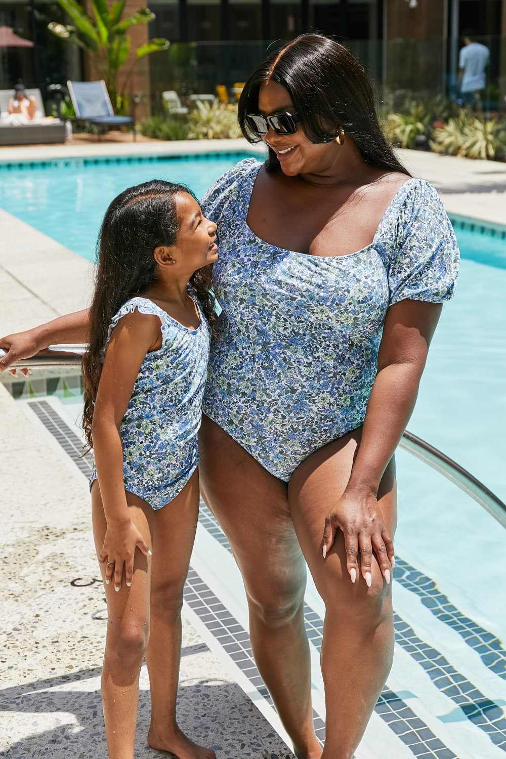 Marina West Swim Salty Air Puff Sleeve One-Piece in Blue with floral pattern, square neck, and belted waist, worn by a woman and child by the pool.