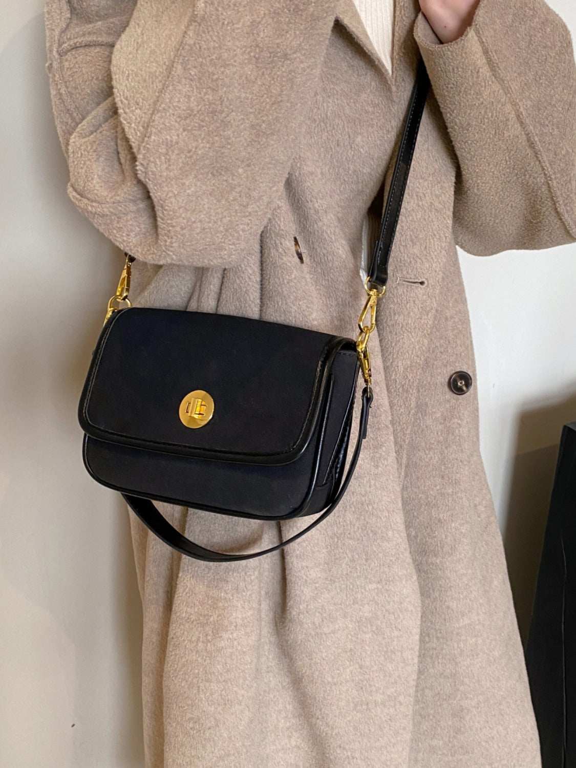 Small PU leather suede twist-lock shoulder bag in black, worn with a beige coat.