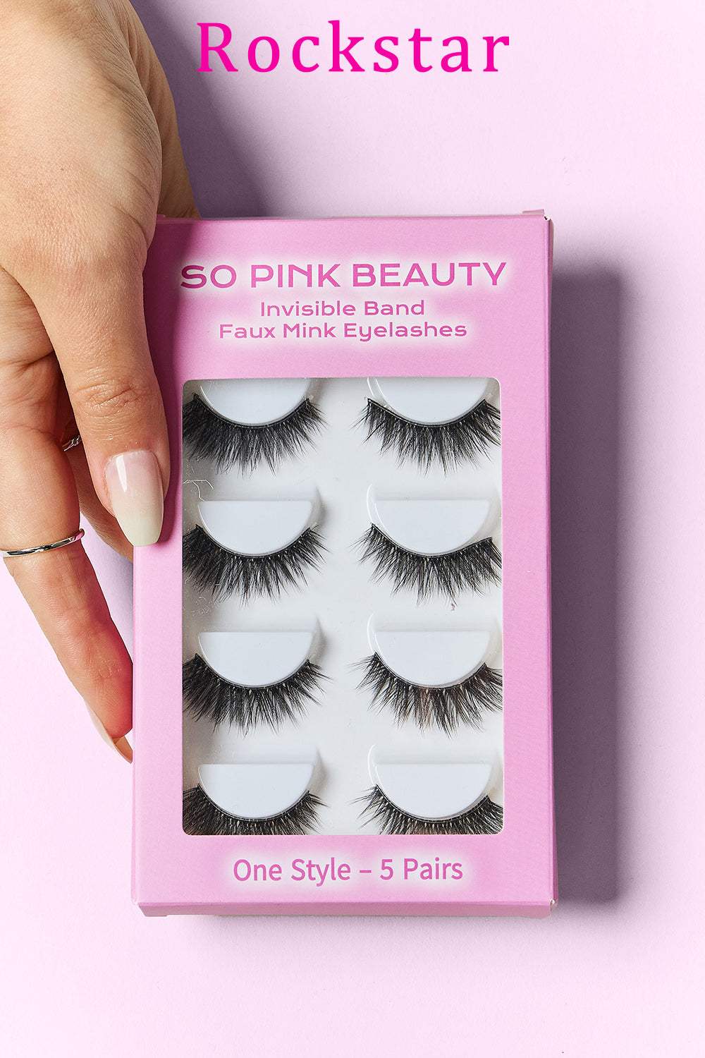 SO PINK BEAUTY Faux Mink Eyelashes 5 Pairs in packaging with a hand holding the box against a pink background.