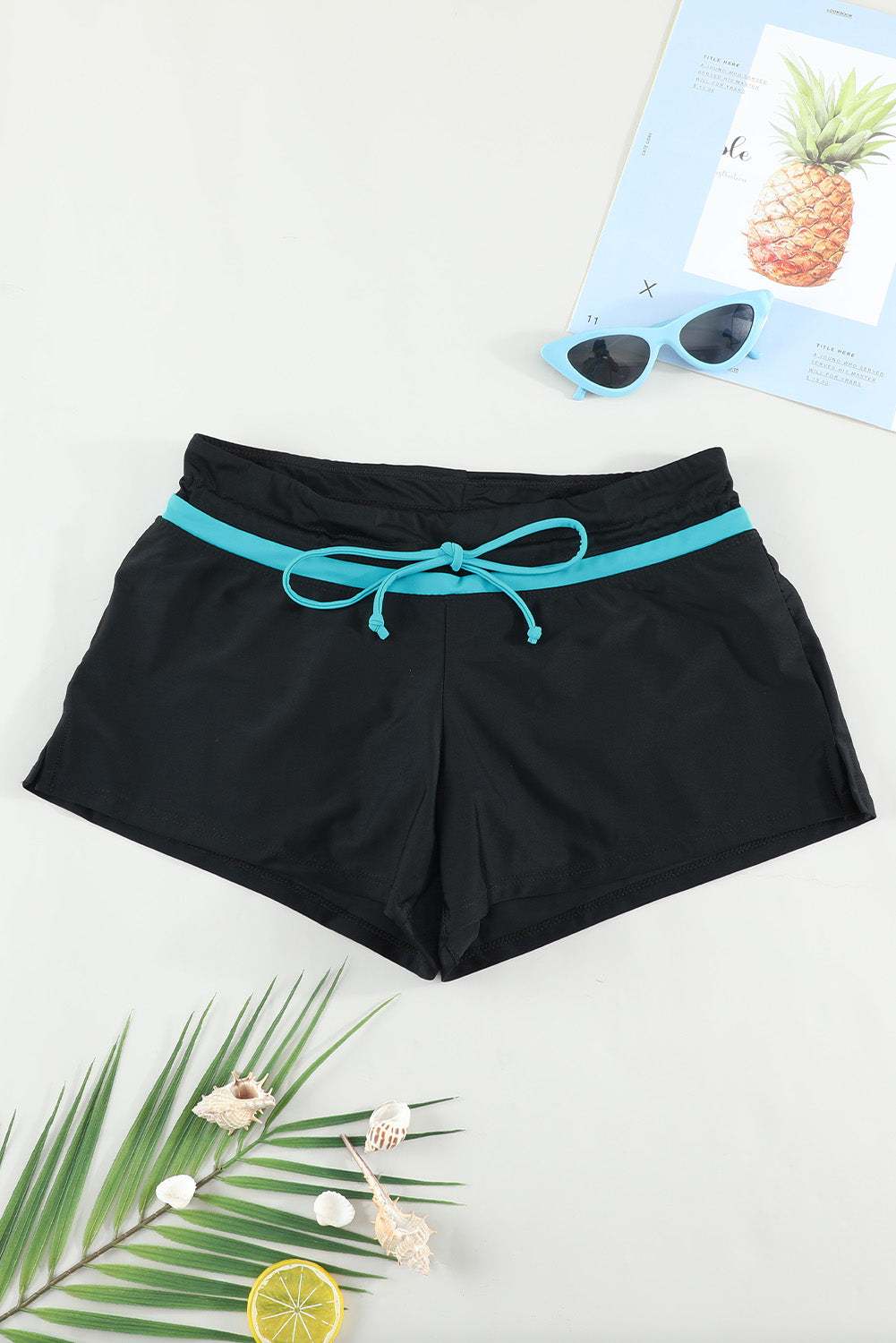 Full size drawstring swim shorts in black with a blue tie, surrounded by tropical decor.