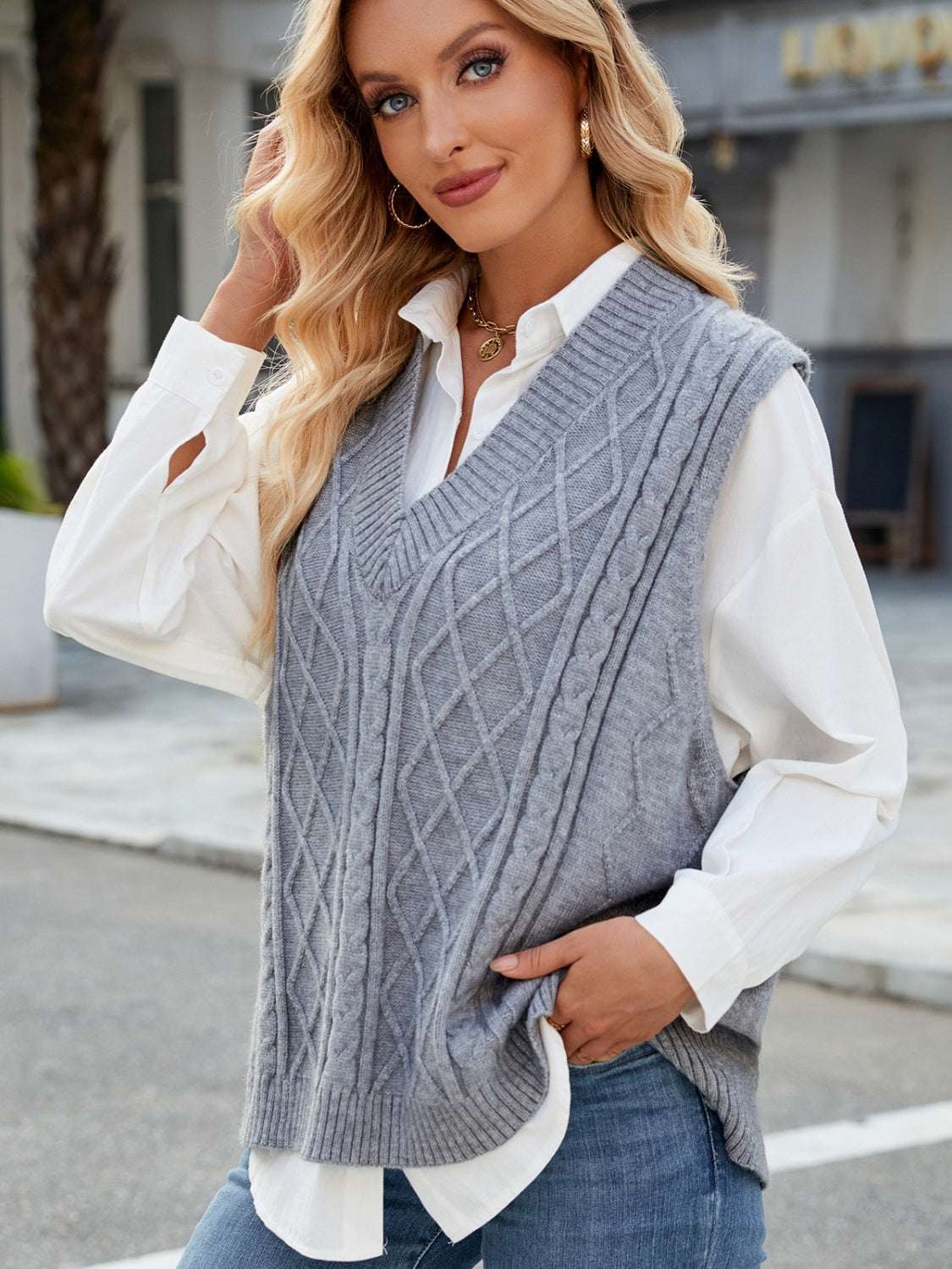 Cable knit V-neck sweater vest in gray, worn over a white blouse.