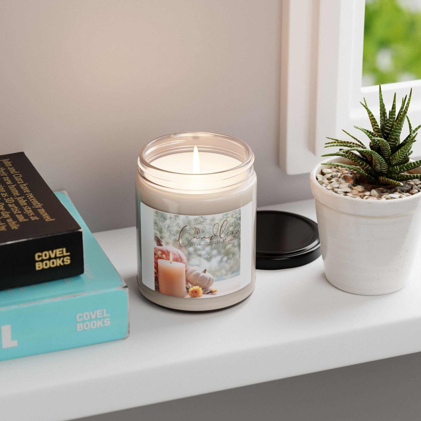 Locket scented soy candle in reusable glass vessel, from Securing Secrets Boutique LLC, on a table next to books and a plant.