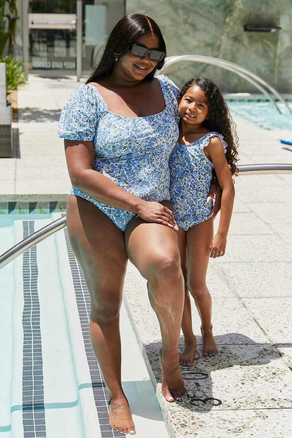 Woman and child wearing blue floral Marina West Swim Salty Air puff sleeve swimsuits by the pool.