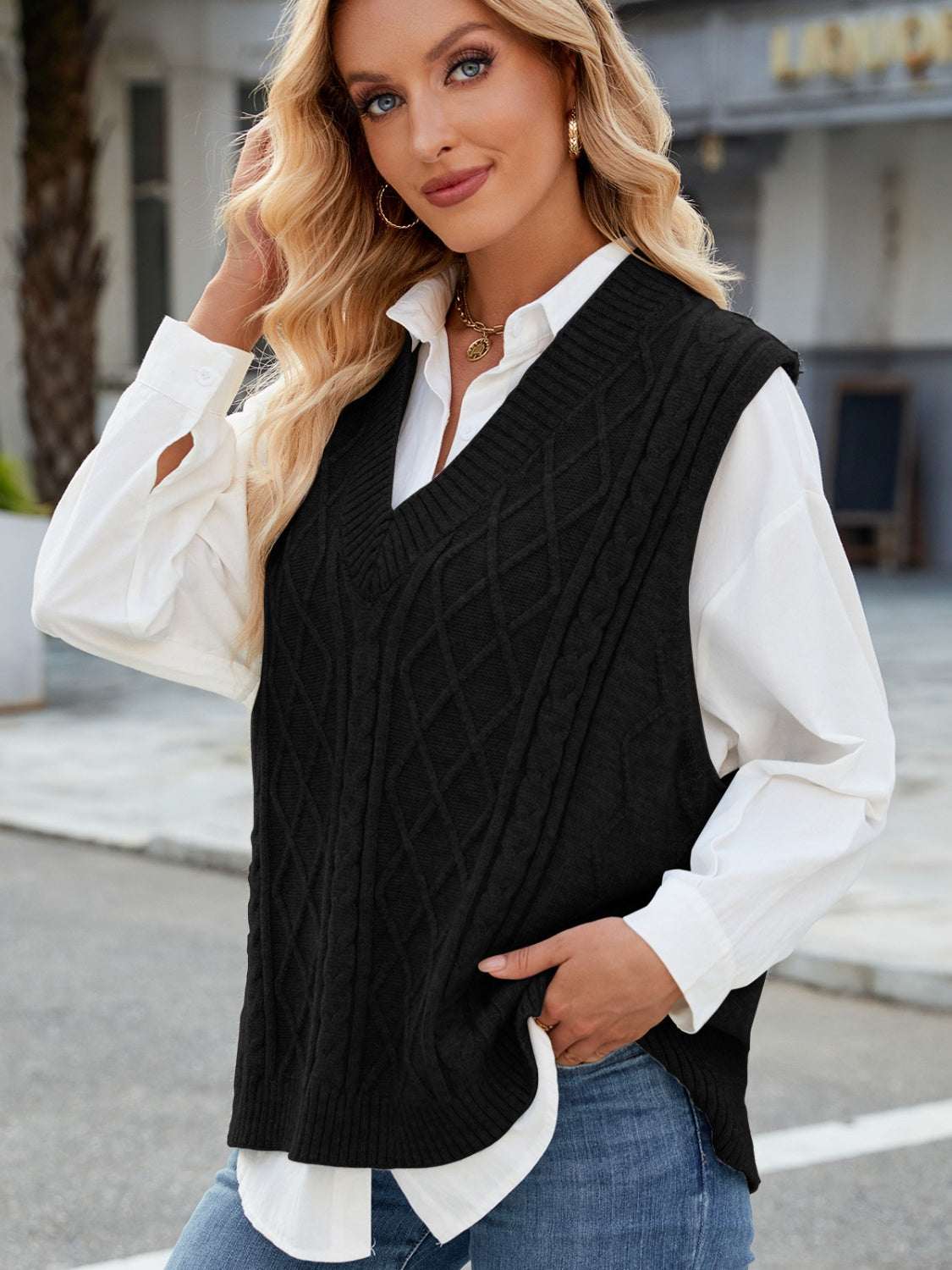 Black cable knit V-neck sweater vest worn over a white shirt.