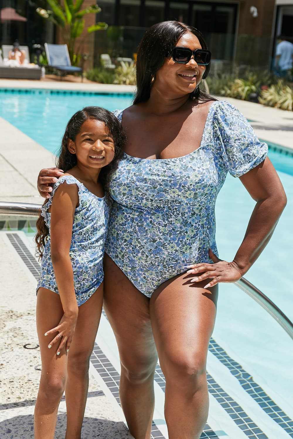 Mother and daughter wearing Marina West Swim Salty Air Puff Sleeve One-Piece swimsuits in blue floral pattern by a pool.