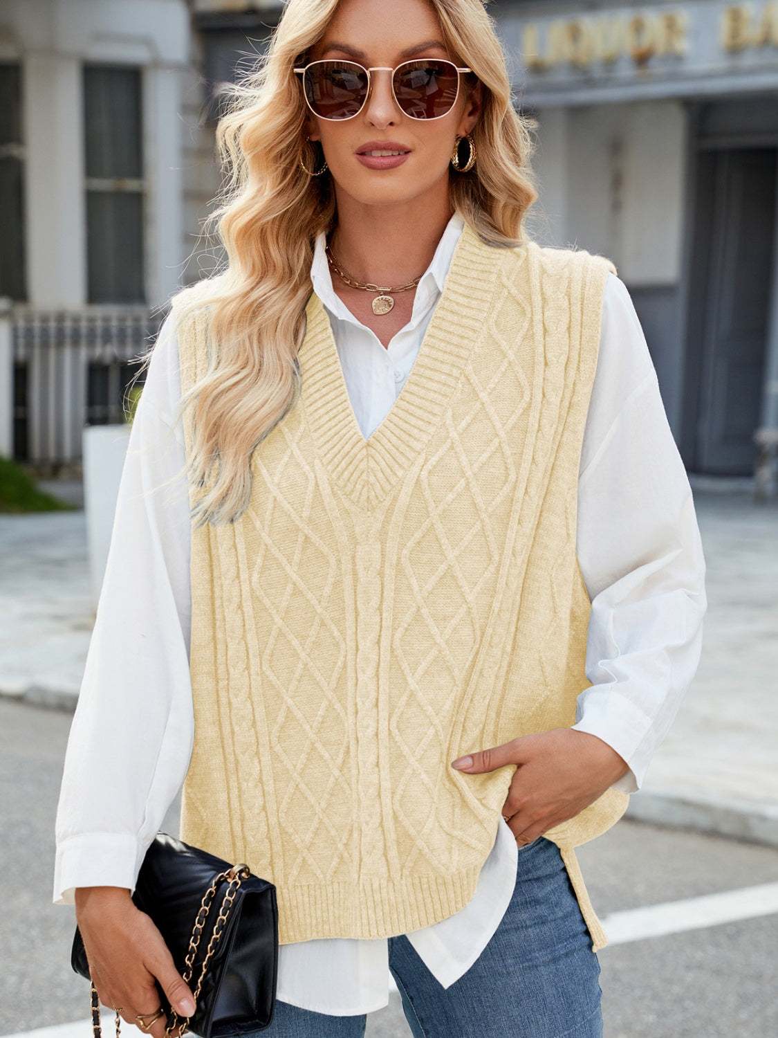 Cable knit V-neck sweater vest in cream, worn over a white shirt with jeans.