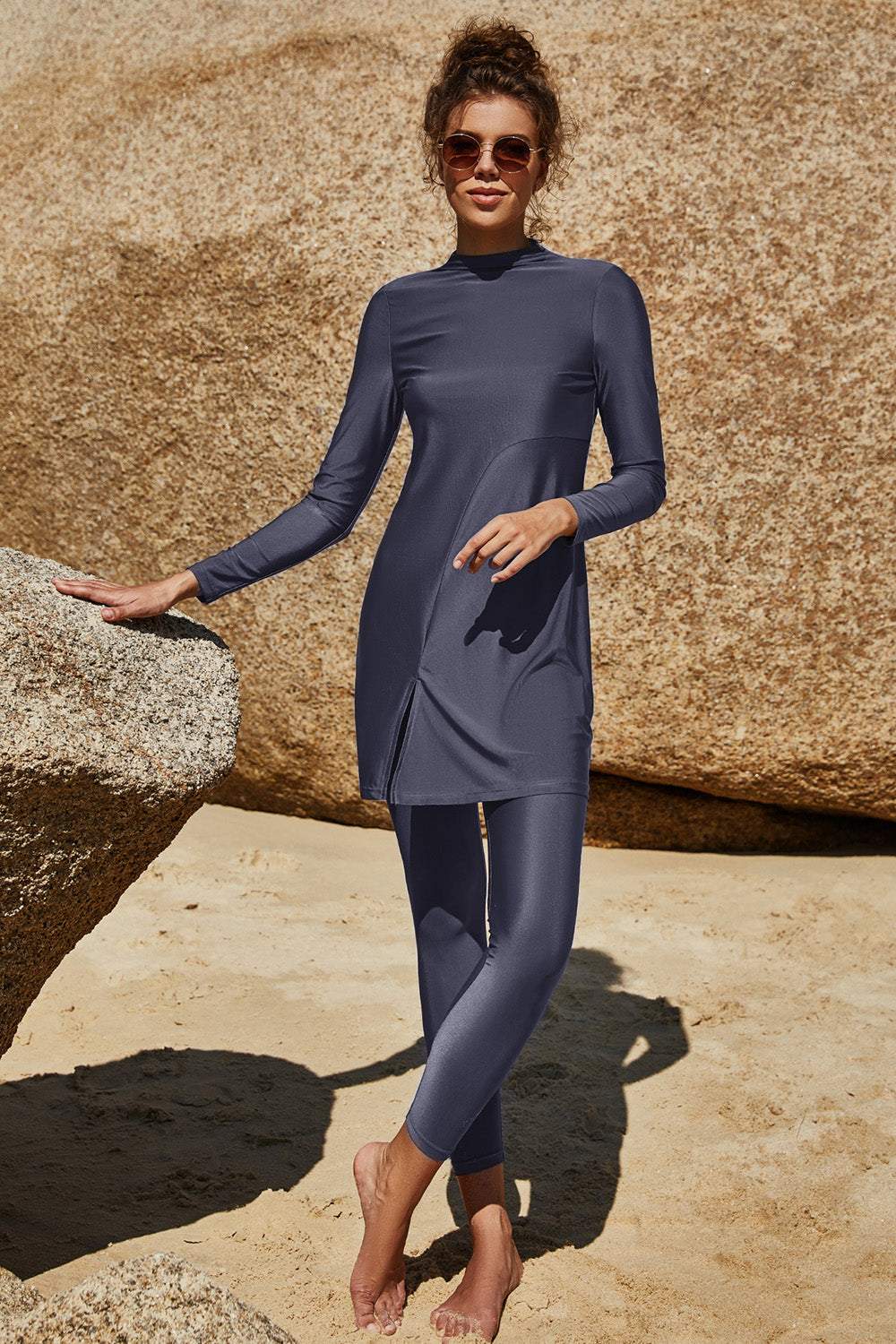 Slit mock neck long sleeve top and pants swim set in a blue-grey color worn by a model on a beach.