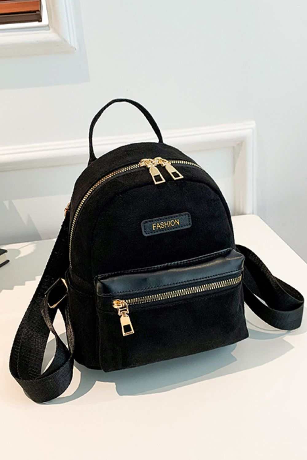 Small black suede backpack with adjustable straps and gold zippers.