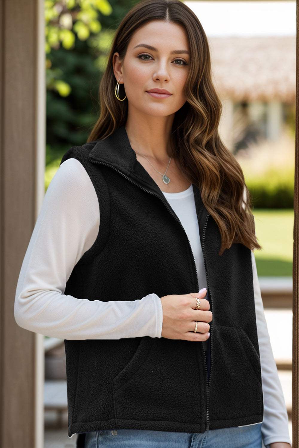 Woman wearing a black zip-up vest coat with pockets over a long-sleeve white top.