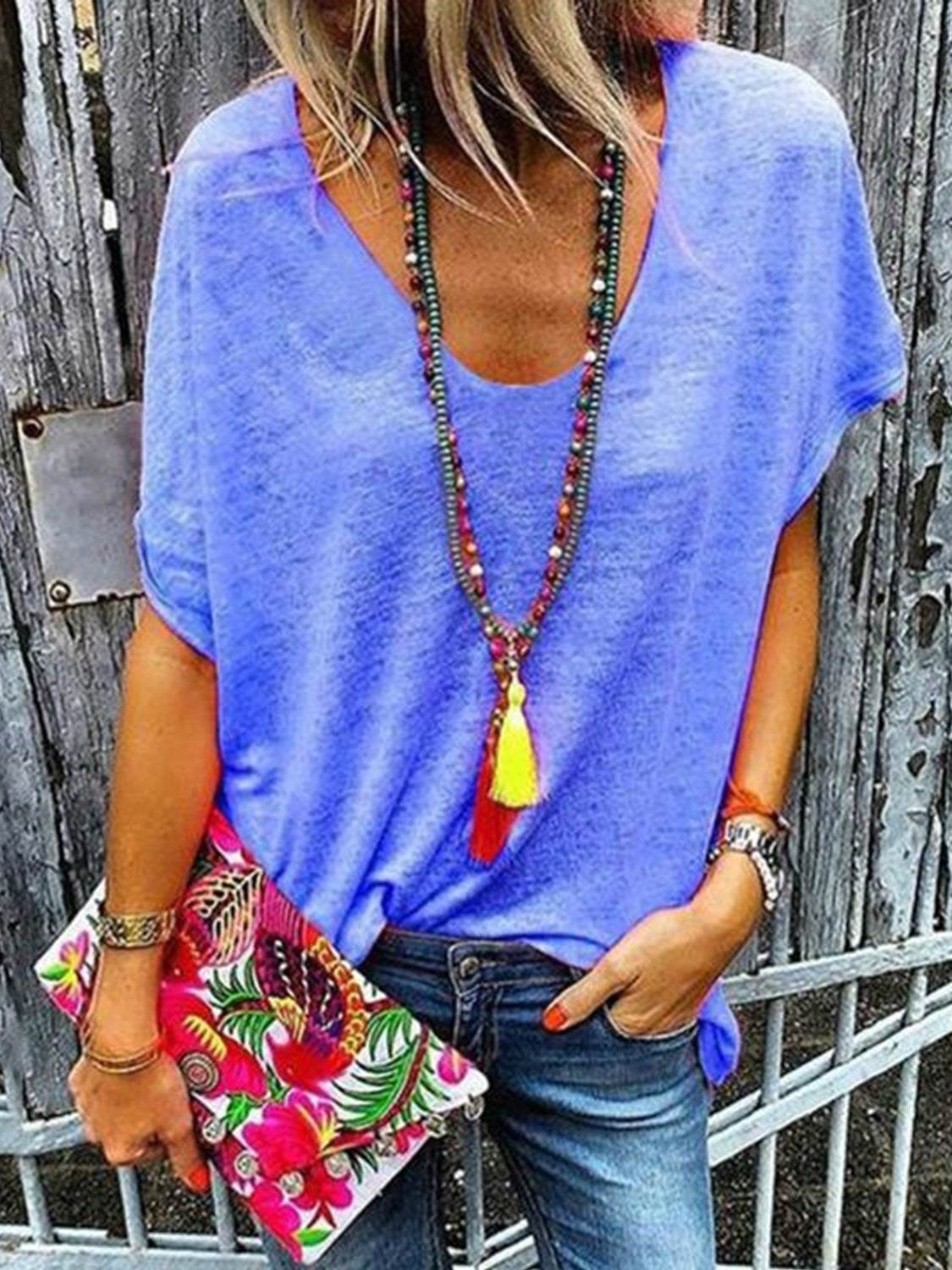 Woman wearing full size scoop neck short sleeve t-shirt in blue, holding a colorful clutch.