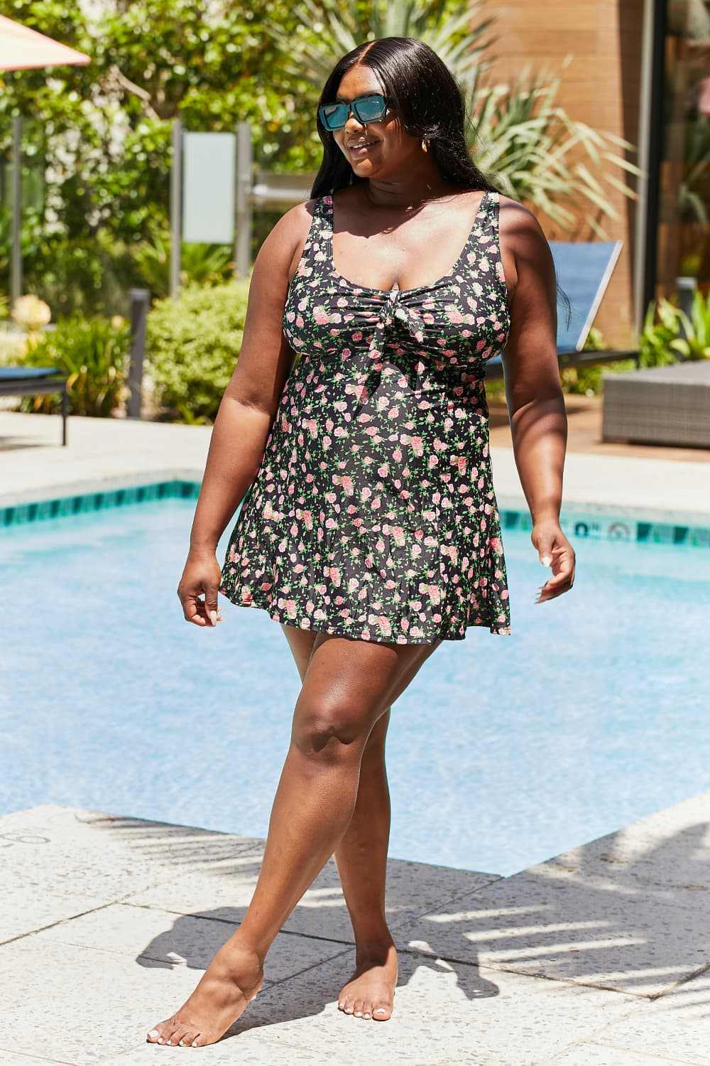 Plus-size woman wearing Marina West Swim Full Size Clear Waters Swim Dress in Black Roses by a pool.