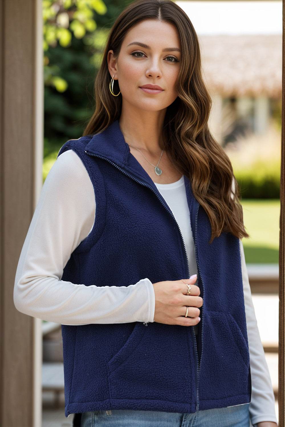 Navy zip up vest coat with pockets and sleeveless design, worn over a white long-sleeve top.