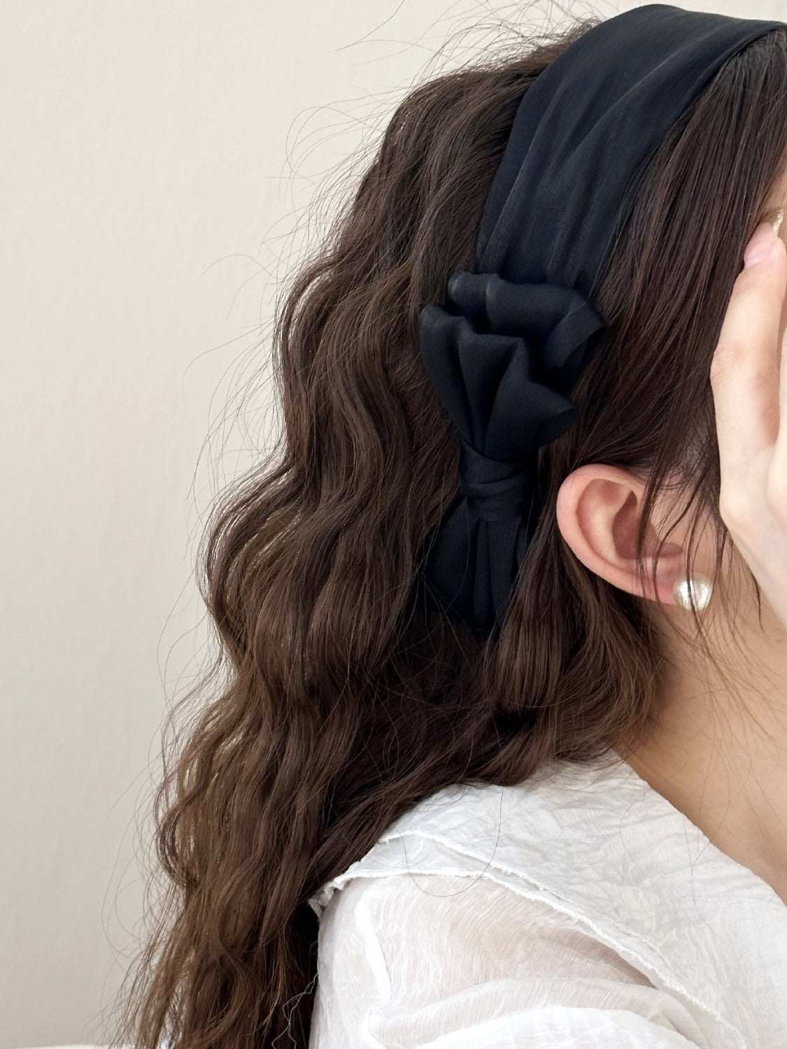 Wide polyester headband with bow design, worn on wavy hair.