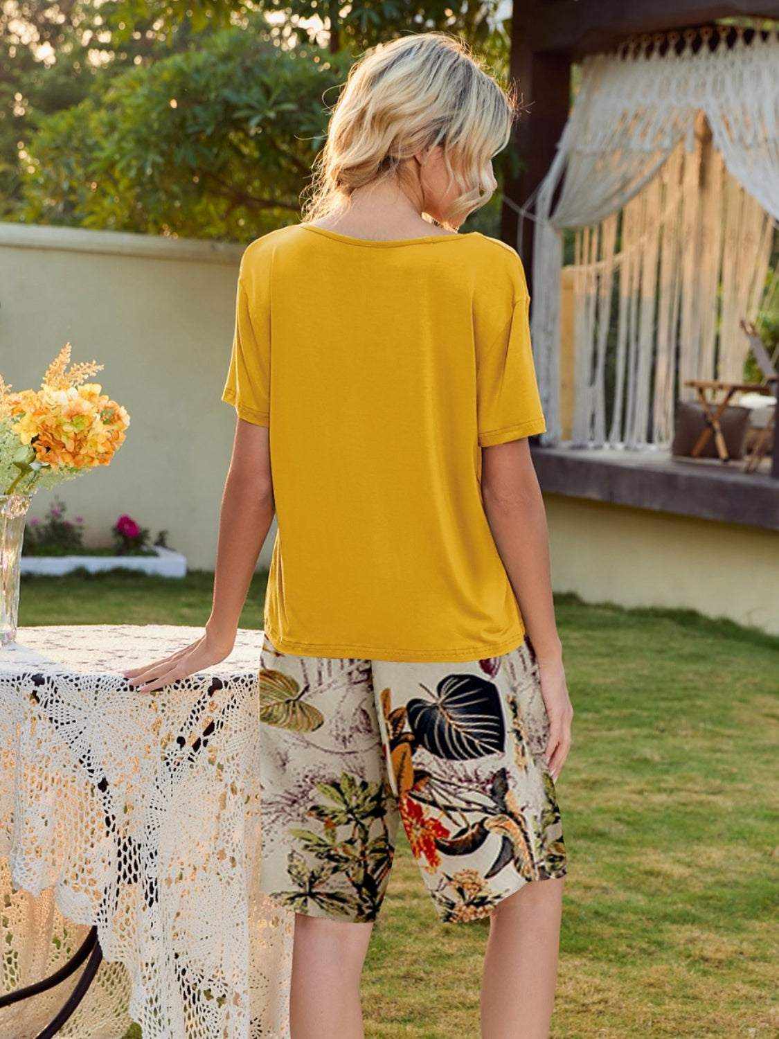 Yellow short sleeve top and floral printed shorts lounge set in a garden setting.