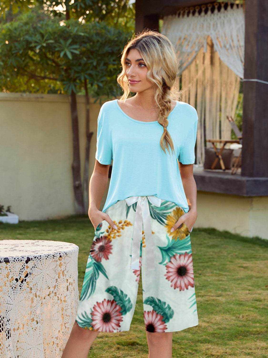 Woman wearing a light blue short sleeve top with colorful printed shorts lounge set, standing outdoors.