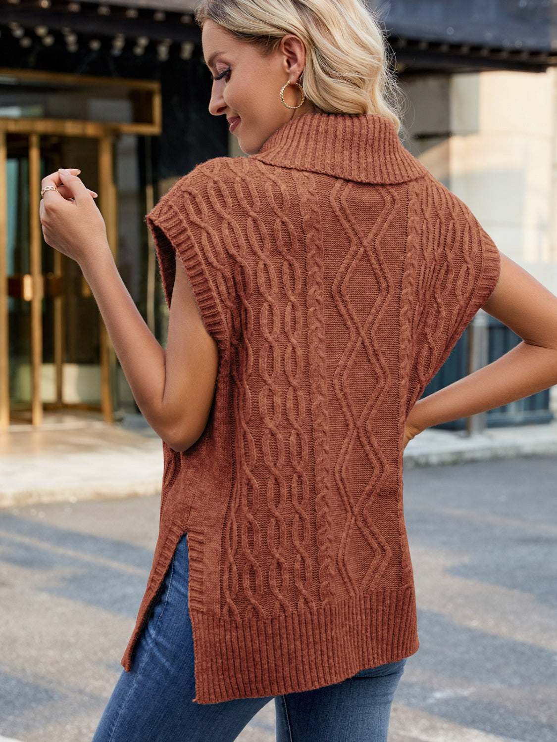 Side slit turtleneck sweater vest in brown with cable knit design, worn by woman.