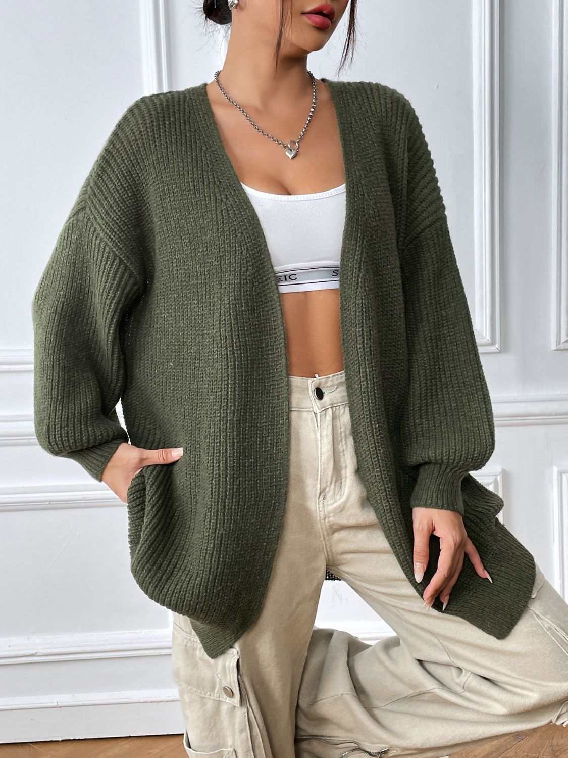 Olive green open front long sleeve cardigan worn over a white crop top and beige pants.